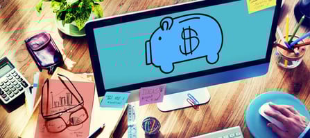 Imagem mostra um computador com um desenho de cofre em formato de porco. Uma mão do lado esquerdo mexendo no computador e postits com anotações. 